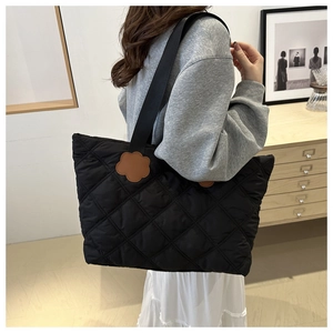 Detail of black quilted tote bag featuring a brown floral leather patch and diamond pattern