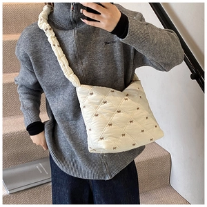 Detail of white quilted tote bag featuring brown bow prints and pleated shoulder strap