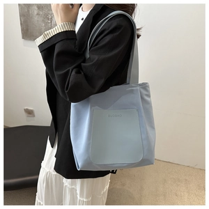 Detail view of the light blue nylon tote bag worn by a model in a minimal setting