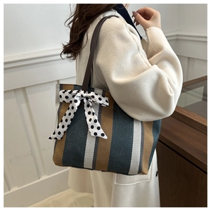 Polished striped canvas tote bag with a polka dot bow worn by a model in beige coat
