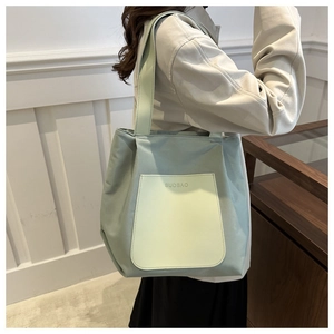 Detail of a sage green tote bag with yellow pocket shown on model against wooden paneling