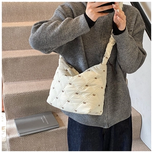 Close-up of quilted beige tote bag with brown bow embroidery on a textured soft material