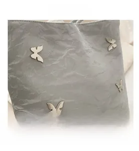 Vue détaillée du sac gris à texture plissée et accents de papillons métalliques