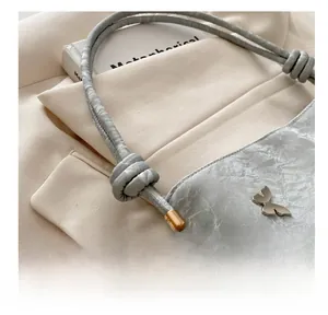 Détail du sac gris argenté avec bandoulière nouée et breloque papillon en métal