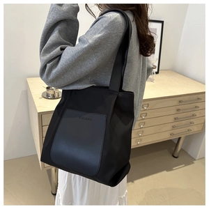 Detail of minimalist black nylon tote bag with leather pocket and branded embossing