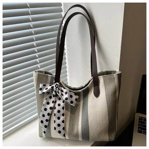 Detail of grey striped woven tote bag with a polka dot silk bow and brown leather handles