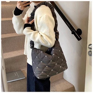 Detailed view of dark grey quilted fabric with white bow embroidery and ruffled shoulder strap