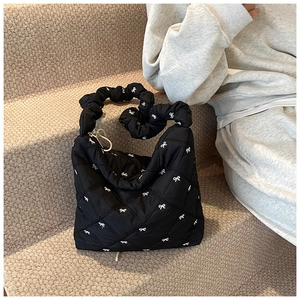 Detail of black quilted tote bag with white bow embroidery and ruffled handle