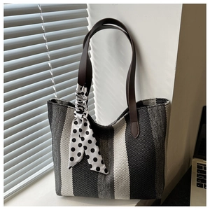 Detail of striped woven tote bag with brown leather handles and decorative polka dot scarf