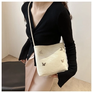 Détail du sac bandoulière crème avec papillons en métal et texture plissée porté par mannequin