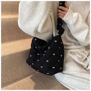 Detail of black quilted nylon tote bag featuring white bow embroidery and ruffled strap