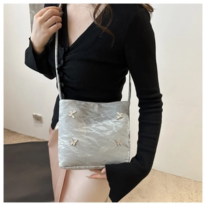Détail d'un sac bandoulière gris texturé avec ornements papillon et finition brillante chic