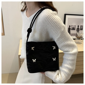Détail du sac plissé noir avec breloques papillon argentées et bandoulière en corde