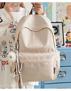 Detailansicht eines karierten Canvas-Rucksacks mit Reißverschlusstasche und Plüschball