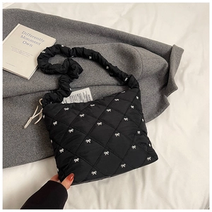 Detail view of black quilted tote bag with white embroidered bows and ruched shoulder strap