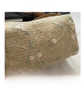 Detailed macro shot of beige straw woven bag with delicate floral embroidery and leaf patterns