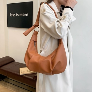 Detail of caramel pleated dumpling bag featuring wide knotted strap and metal hardware