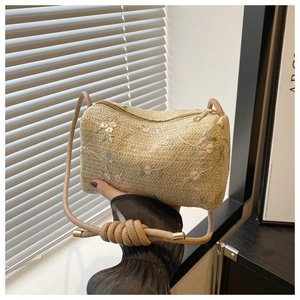 Detailed close-up of woven straw bag with floral embroidery and gold metal zipper hardware