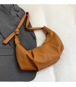 Close-up of brown pebbled leather dumpling bag featuring knot detail and metal ring