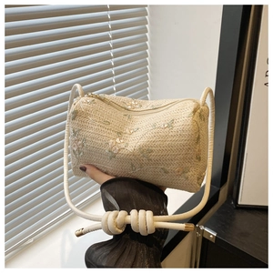 Detail of cream straw cylinder bag with floral embroidery and knotted rope shoulder strap