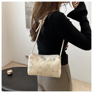 Chic cylindrical straw crossbody bag with floral embroidery shown on a model