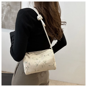 Detail of woven straw bag featuring floral embroidery and white rope shoulder strap
