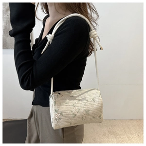 Detail view of woven cylinder bag featuring pink and green floral embroidery and cord strap