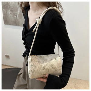 Detail of cream woven cylinder bag featuring floral embroidery and knotted rope strap