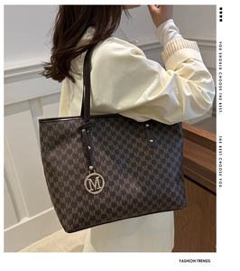 Close-up of printed lettering pattern and golden metal logo tag on the tote bag