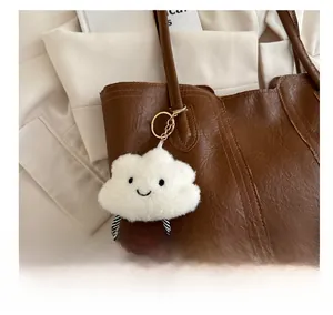 Nahaufnahme eines flauschigen Wolkenanhängers mit Gesicht und Goldclip an Ledertasche
