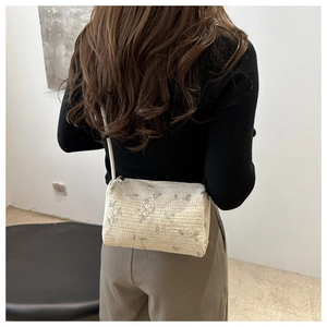 Detail of embroidered straw barrel bag with delicate floral patterns and crossbody strap