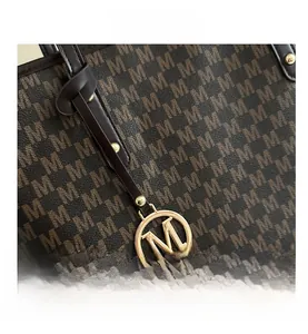 Close-up of deep brown tote bag with M letter pattern and golden metal M charm logo