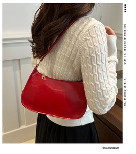 Fashionable red patent leather crescent hobo bag shown over a white cable-knit sweater