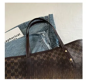 Close-up of deep brown tote bag with M-letter pattern, metal rivets, and thin straps