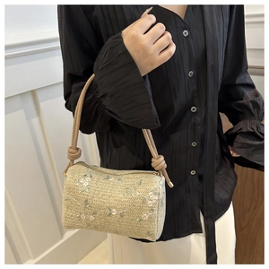 Close-up of beige woven barrel bag featuring delicate floral embroidery and knot detail