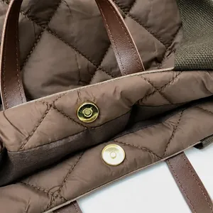 Detail shot of the golden magnetic buckle closure on a brown quilted puffer crossbody bag