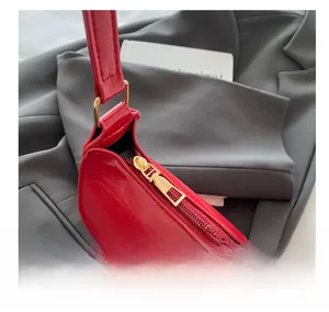 Detail of the golden metal zipper on the glossy red leather crescent shoulder bag