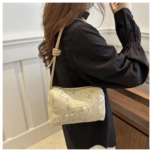 Detail of cylindrical straw bag featuring floral embroidery and a knotted beige shoulder strap