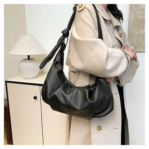 Close-up of a black pleated crescent shoulder bag featuring a unique large knot on the strap