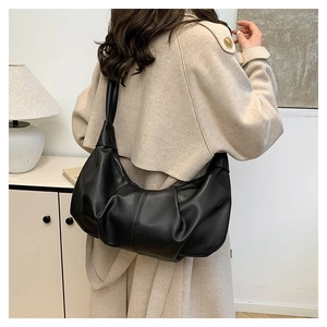 Detail of a large black pleated crescent bag worn over a beige coat for daily commuting