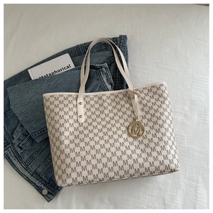 Detail of cream tote bag with grey M-letter print and gold metal charm accessory