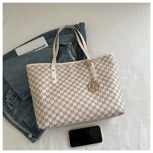 Flat lay of cream monogram tote bag with gold M-pendant and lifestyle accessories