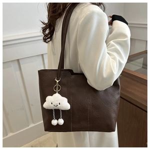 Detail der dunkelbraunen Leder-Shopper-Tasche mit weißem Wolken-Plüsch-Anhänger