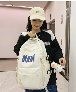 Close-up of cream backpack featuring MRM logo and cute plush duck pendant detail