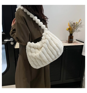 Detail of white faux fur tote bag featuring pleated texture and fuzzy pom-pom shoulder strap