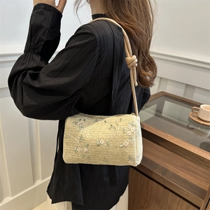 Fashionable straw pillow bag with floral embroidery and rope strap shown on model