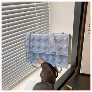 Detail of light blue quilted crossbody bag with silver chain strap and flap closure