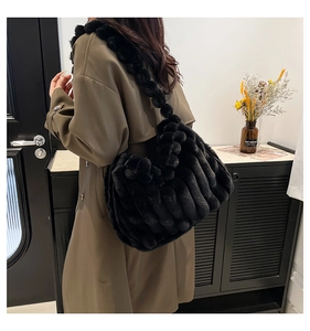 Detail of a large black faux fur tote bag with wavy texture and plush ball strap
