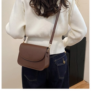 Sac bandoulière en cuir marron mat avec texte FASHION BAGS porté sur un pull en tricot blanc