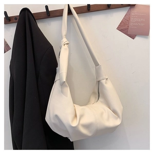 Detail showing creamy white pebbled leather texture and knotted strap on crescent bag